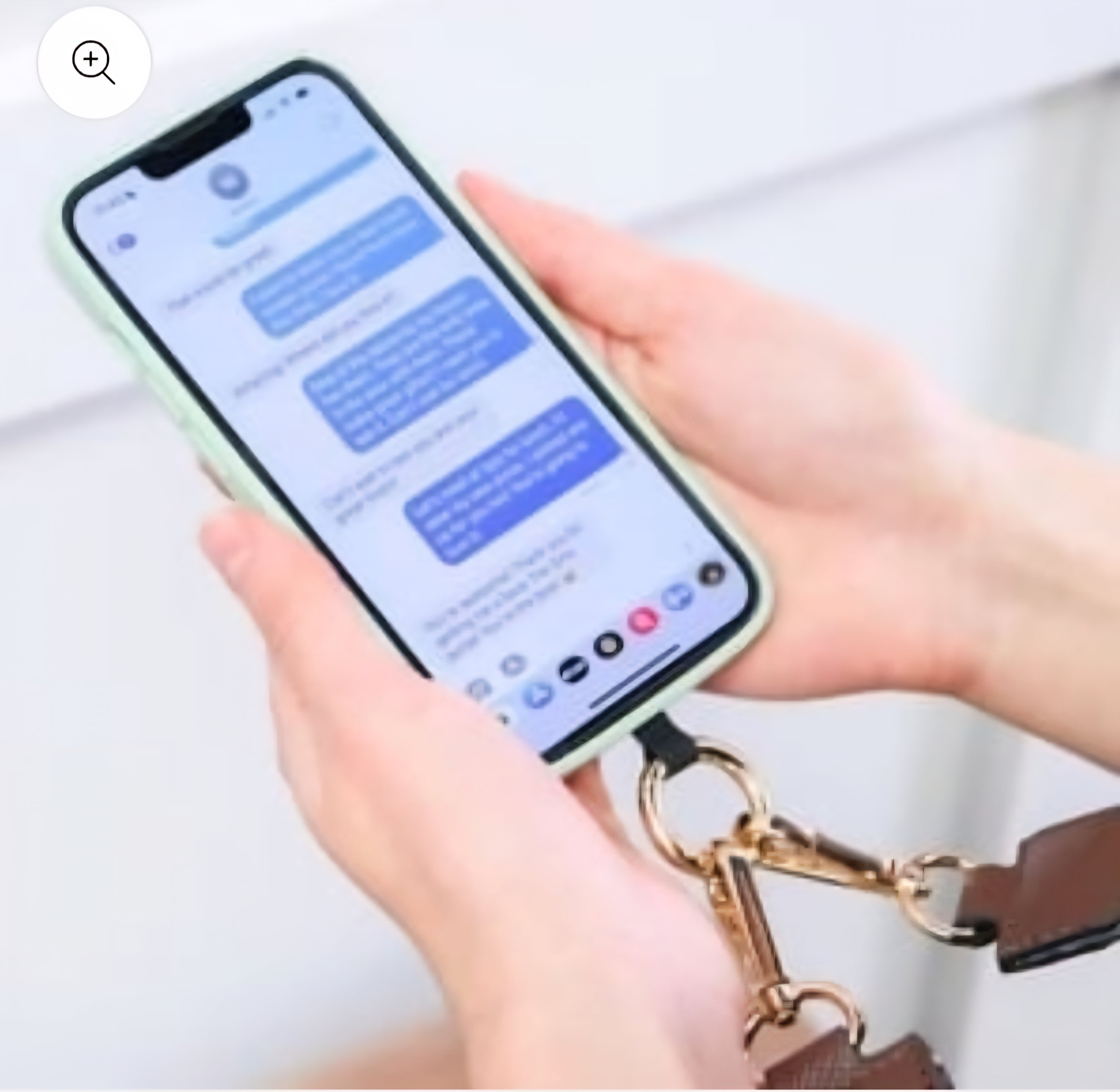 Hands holding a phone with a lanyard, displaying text messages.