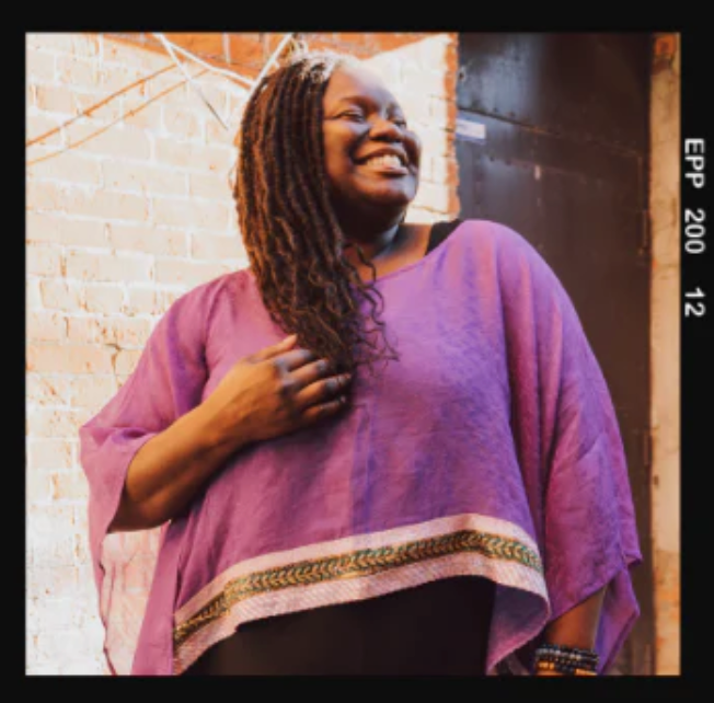 Smiling woman in purple, screenshot from July 19, 2025.