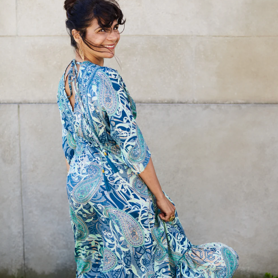 Woman in blue paisley dress, smiling, screenshot August 16, 2025.